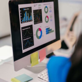 Focused businesswoman analyzes financial data on her computer, using graphs to plan for growth. Her cluttered desk shows her dedication to success