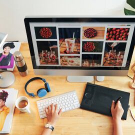 Directly above view of unrecognizable designer choosing photos for magazine page on modern computer in office
