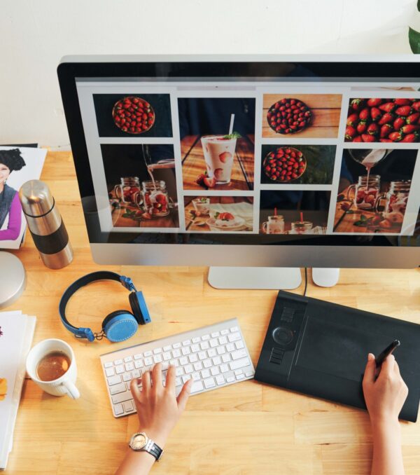 Directly above view of unrecognizable designer choosing photos for magazine page on modern computer in office